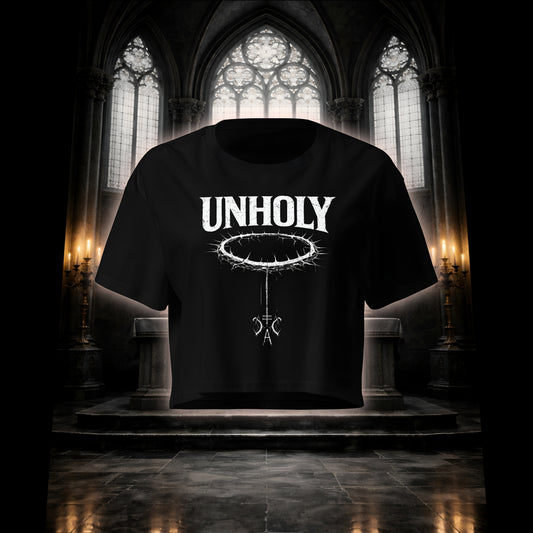 Schwarzes Crop Top mit weißem Unholy Schriftzug und Dornenkranz-Design, freigestellt vor einem düsteren Kirchenaltar mit Kerzen.